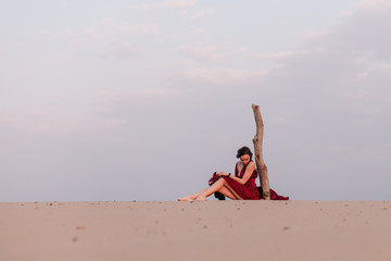 Young girl in a beautiful red dress sits in the wind in the desert