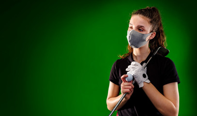 Girl golf player with protective mask waits for his turn to make his best shot, isolated on green background