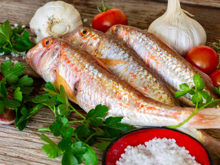 red mullet on an old wooden board background with typical ingredients of an Italian recipe 