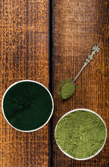 An isolated tablespoon of dried organic wheat grass and spirulina powder, on white rustic background