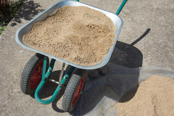 Dirty green wheelbarrow full of sand. Handcart standing in the construction site or household.