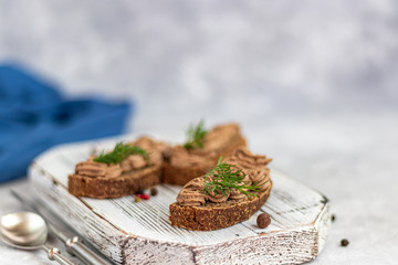 Fresh homemade chicken liver pate with carrots, onions and butter. Garnished with a sprig of dill. Lubricated on bread. On a gray background under concrete.