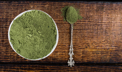 An isolated tablespoon of dried organic wheat grass and spirulina powder, on white rustic background