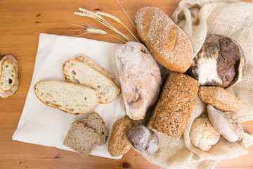 Slices and toasts, loafs and buns of homemade wheat and rye bread with burlap sack and ears. Top view. Wooden table background. Bakery or healthy breakfast concept