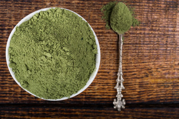An isolated tablespoon of dried organic wheat grass and spirulina powder, on white rustic background