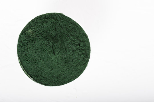 An isolated tablespoon of dried organic spirulina algae powder, on white or rustic background.