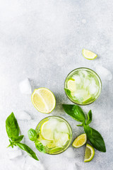 Summer homemade lemonade made from lime, lemon, cucumber and basil with ice in glass on an old concrete background. Selective focus.
