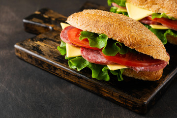 Healthy sandwiches with bran bread, cheese, lettuce, tomato and sliced salami on a rustic wooden stand. Breakfast concept. Top view.