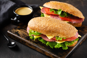 Healthy sandwiches with bran bread, cheese, lettuce, tomato and sliced salami on a rustic wooden stand. Breakfast concept. Top view.