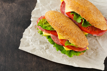 Healthy sandwiches with bran bread, cheese, lettuce, tomato and sliced salami on a rustic wooden stand. Breakfast concept. Top view.