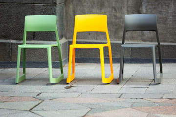 Three multi-colored chairs standing on the sidewalk
