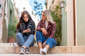 couple of attractive girls sitting on the street dressed in casual clothes.