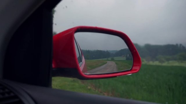 Ein Rotes Auto f&auml;hrt durch am Waldrand &uuml;ber eine Landstra&szlig;e mit Blick durch den Spiegel