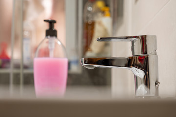 Grifo de un lavabo con jabón de manos al fondo en un cuarto de baño.