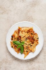 Pasta Maltagliati with classic tomato sauce, parmesan and basil on a rustic concrete light table background. Traditional Italian dish serving. Top view.