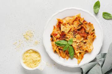 Pasta Maltagliati with classic tomato sauce, parmesan and basil on a rustic concrete light table background. Traditional Italian dish serving. Top view.