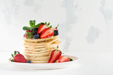 Stack of homemade little pancakes with honey, fresh strawberries and sauce on light wooden background. Selective focus.