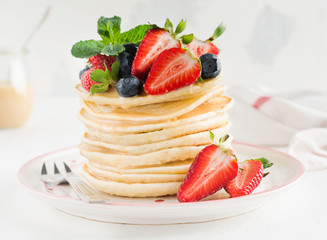 Stack of homemade little pancakes with honey, fresh strawberries and sauce on light wooden background. Selective focus.