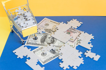 Shopping cart full of jigsaw puzzle on money dollar background, Business solution concept.dollar banknote under unfinished white jigsaw puzzle. USA or world economy crisis situation currency war