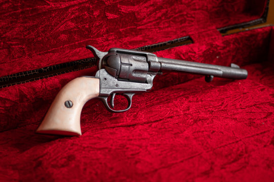 Antiguo rev&oacute;lver del oeste con cachas blancas sobre terciopelo rojo