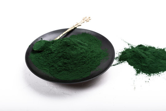 An isolated tablespoon of dried organic spirulina algae powder, on white or rustic background.