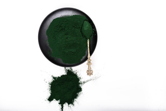 An isolated tablespoon of dried organic spirulina algae powder, on white or rustic background.