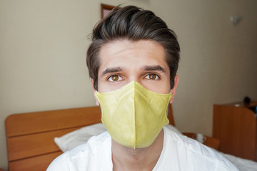 Portrait of a young attractive man wearing a face mask in his bedroom 
