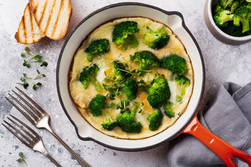 Omelette with broccoli and green young onions on red cast iron pan on old gray concrete background. Top view.