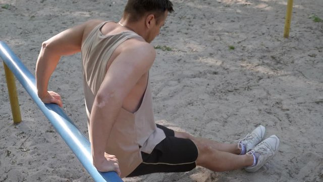 An athlete street workout on the beach. Triceps exercise on a bar