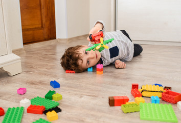 Happy little boy kid is lying on the wood floor and playing