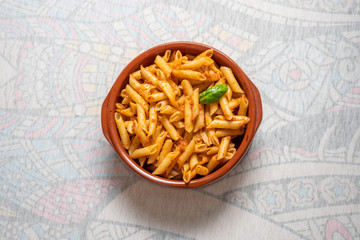 Cazuela de barro con macarrones al pesto rojo sobre fondo blanco