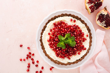 Homemade dessert chocolate tart with coconut cream and pomegranate and mint on a pink table background. Top view.