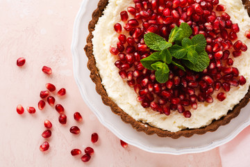 Homemade dessert chocolate tart with coconut cream and pomegranate and mint on a pink table background. Top view.