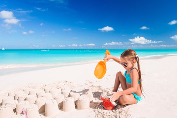 Little girl at tropical white beach making sand castle