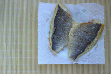 
Fried filet of dorado sea fish lies on a paper towel absorbing excess fat. View from above