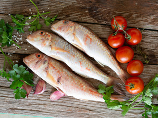 red mullet on an old wooden board background with typical ingredients of an Italian recipe 