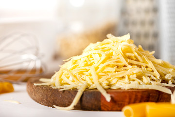 Pile of grated cheese on a cutting board close-up. Cooking pasta with grated cheese. Cheese and kitchen utensils on the table.