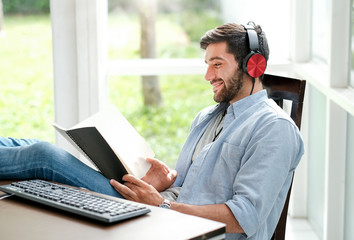 Handsome business man with casual cloth is listening some music from computer in front of computer in glass window room. He looks happy and relax during work from home during corona virus pandemic.