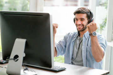 Handsome business man with casual cloth smile and express happy emotion look to monitor of computer in glass window room. He looks enjoy and relax during work from home in corona virus pandemic.