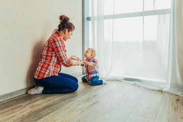 Stay Home Stay Safe. Young mother holding her child. Woman and infant little girl relaxing in white bedroom near windiow indoors. Happy family at home. Young mom playing whith her daughter.