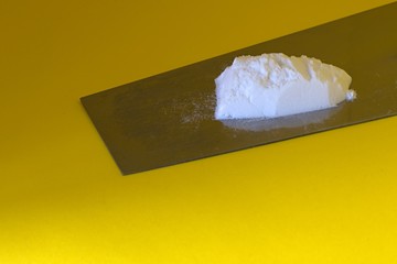 a little bunch of white powder on a metal plate on a yellow background
