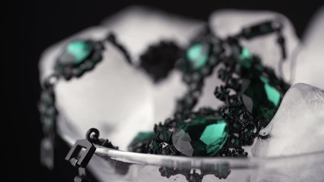 Glass goblet with ice cubes and precious jewelry. Time lapse ice is melting. Close up of an emerald bracelet with ice cubes. Concept for sales and price cuts.