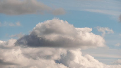 Obraz premium Lush, voluminous, white clouds in a clear blue sky with dark clouds, illuminated by the rays of the sun on a Sunny day.