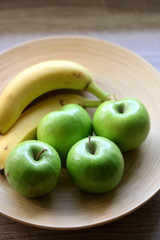 Wooden bowl with green apples and bananas on a table. Selective focus.