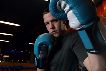 A young strong Thai boxer stands in a combat rack in the gym and looks into the camera. Boxer in...