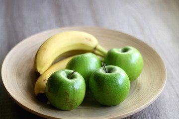 Wooden bowl with green apples and bananas on a table. Selective focus.