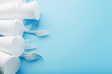 Plastic tableware on a blue background. Disposable forks and glasses with free space.