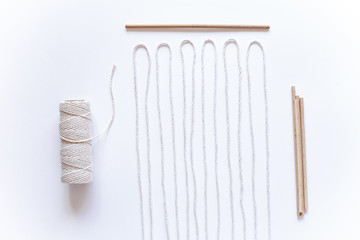 Tools and materials for macrame weaving over white surface. Cotton ropes and sticks from the river,...