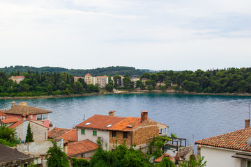 Fototapeta na wymiar View of the Adriatic Sea with the roofs of the typical croatian houses and the green vegetation in the land, in Rovinj, Croatia