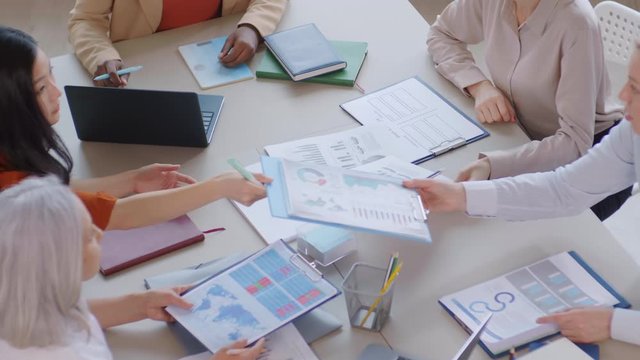 High angle view of five diverse successful businesswomen sitting at desk in the office and analyzing data on different charts